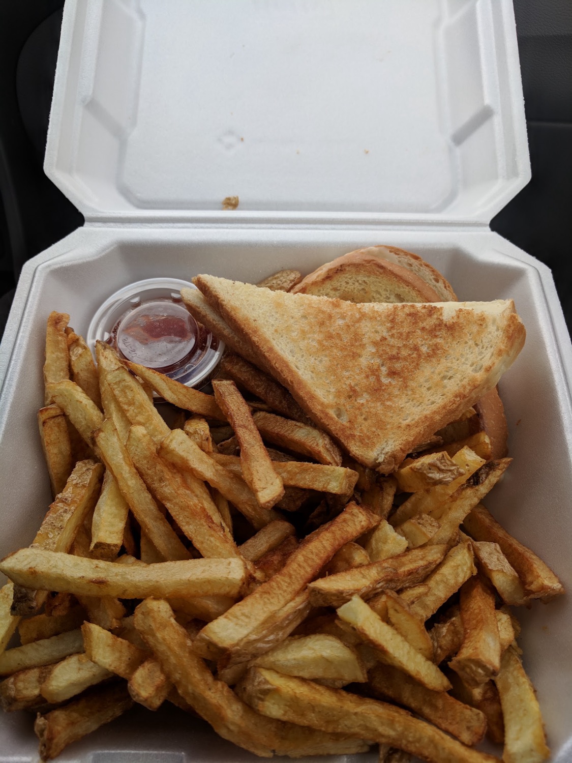 A grilled cheese sandwich cut in triangles with a large side of fries in a takeout box.