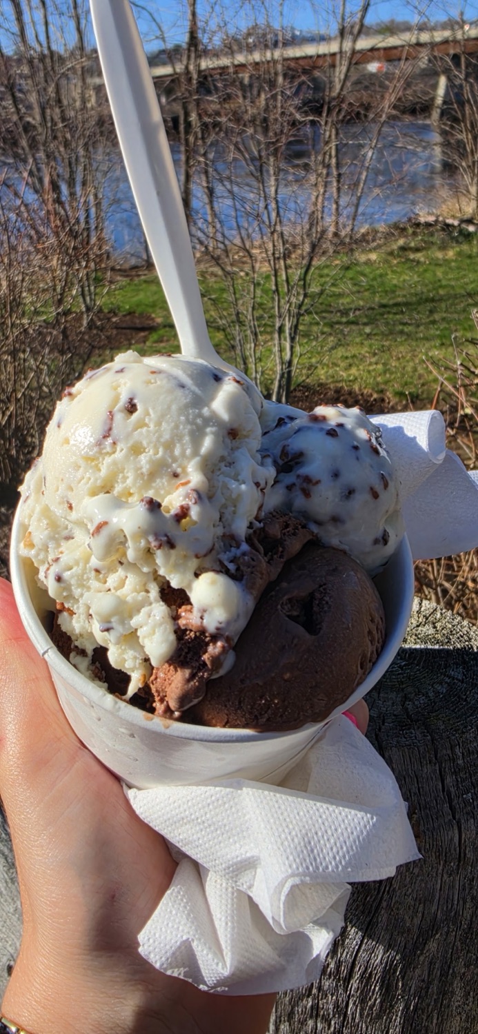 A cup with two scoops of ice cream held up in front of the Penobscot River and a bridge.
