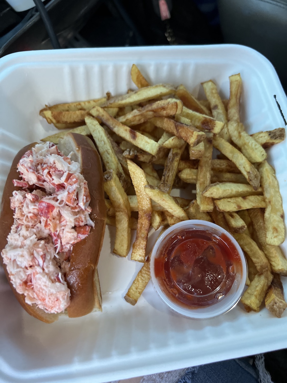 A lobster roll packed with lobster meat next to hand-cut fries and cocktail sauce.